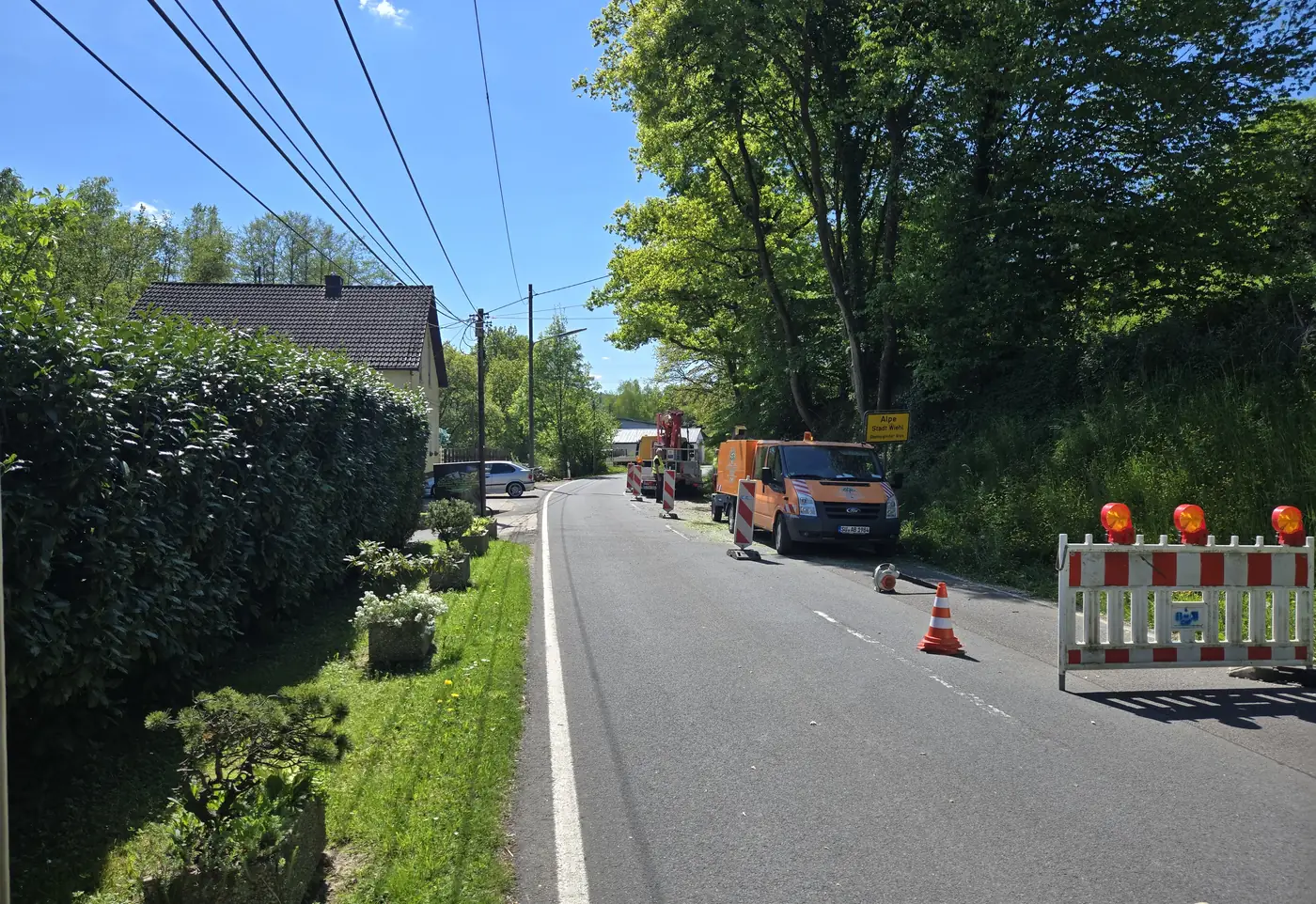 Abgesperrte Durchgangsstraße mit Warnbaken und Arbeitsfahrzeugen während einer Baumfällung
